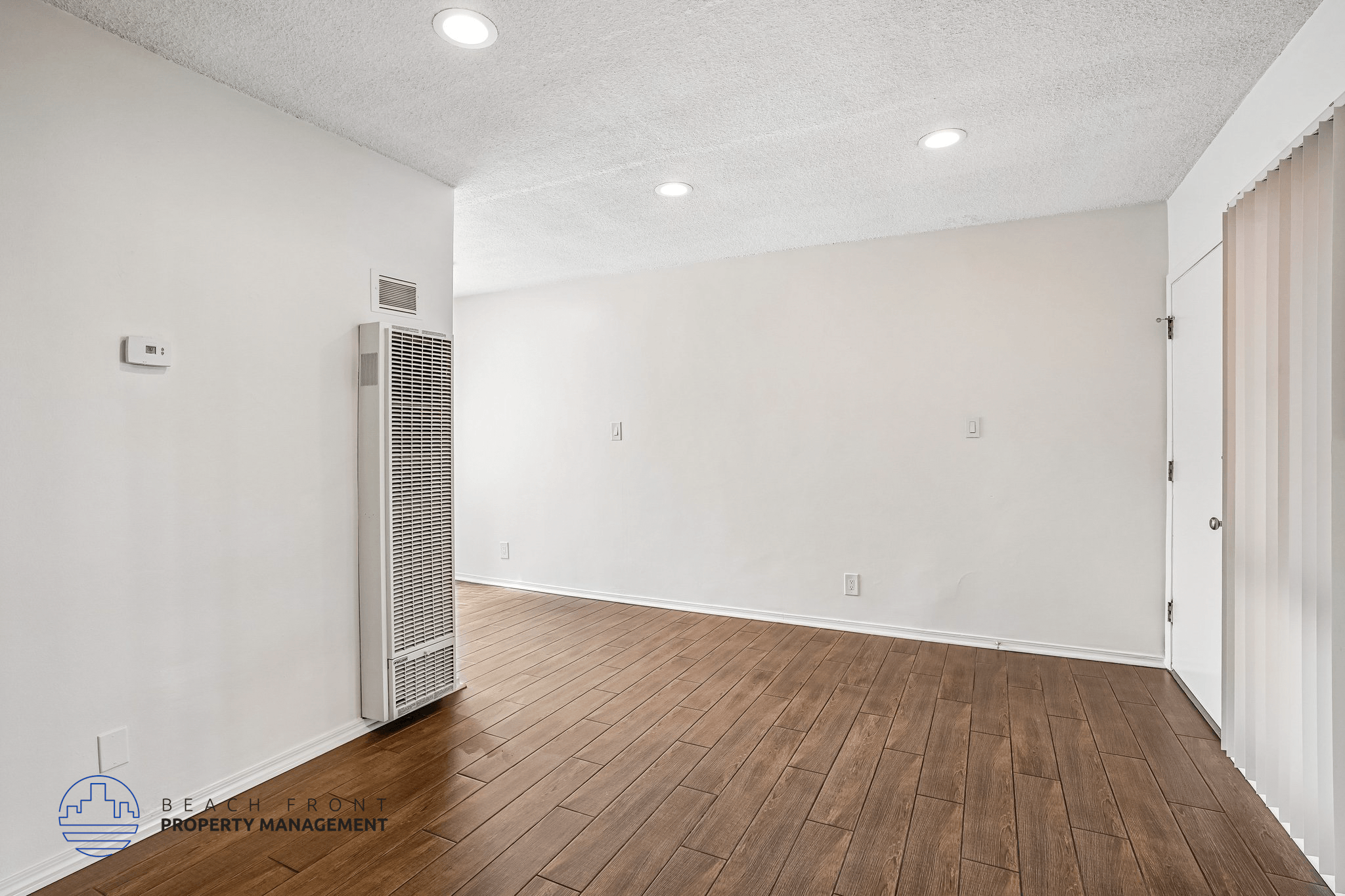 A spacious room with a wood floor and a wall-mounted air conditioning unit.